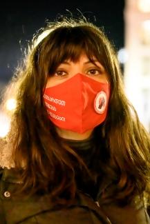 La photo montre Sopo Japaridze, l'une des cofondatrices de l'Union Solidarity Network. Sopo a de longs cheveux bruns, avec une frange, et des yeux bruns, et porte un masque rouge de l'Union du réseau de solidarité. La photo est prise de nuit. 