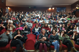 Photo of people sitting on red chairs in a hall