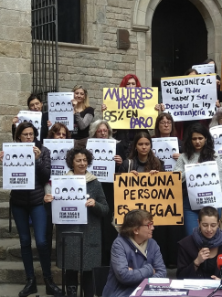 La foto vertical muestra un grupo de mujeres con carteles durante una manifestación con tres personas sentadas