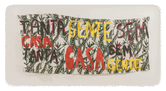 A graphic with green feather patterns on a beige background, text on it in Portuguese says “Tanta Gente sem casa. tanta casa sem gente” which means "So many people without a home,  so many homes without people"